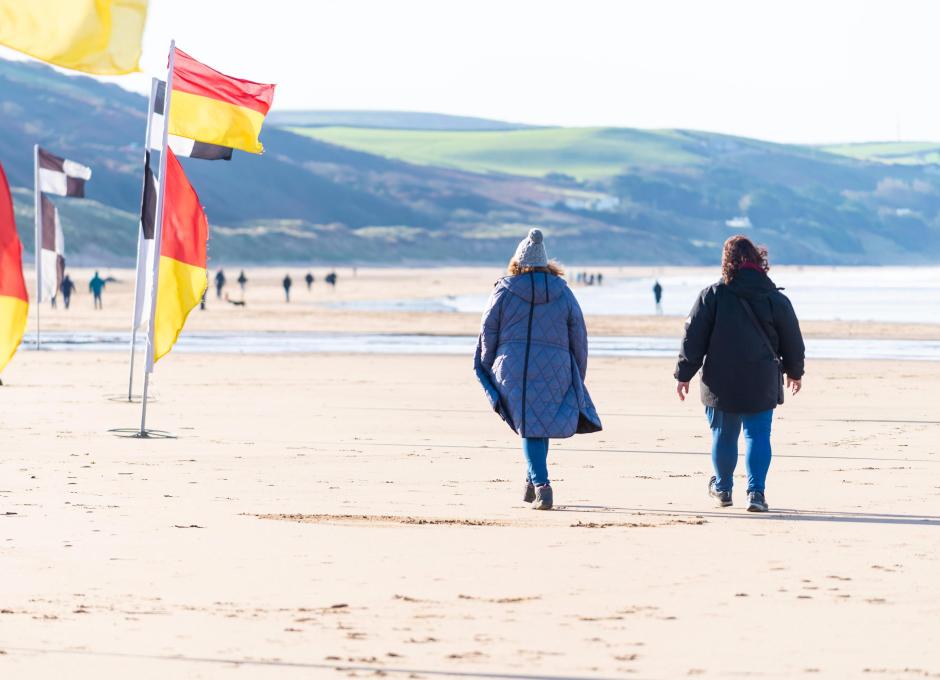 Two guests from Woolacombe Sands Holiday Park walking by RNLI Lifeguard Flags on Woolacombe Beach