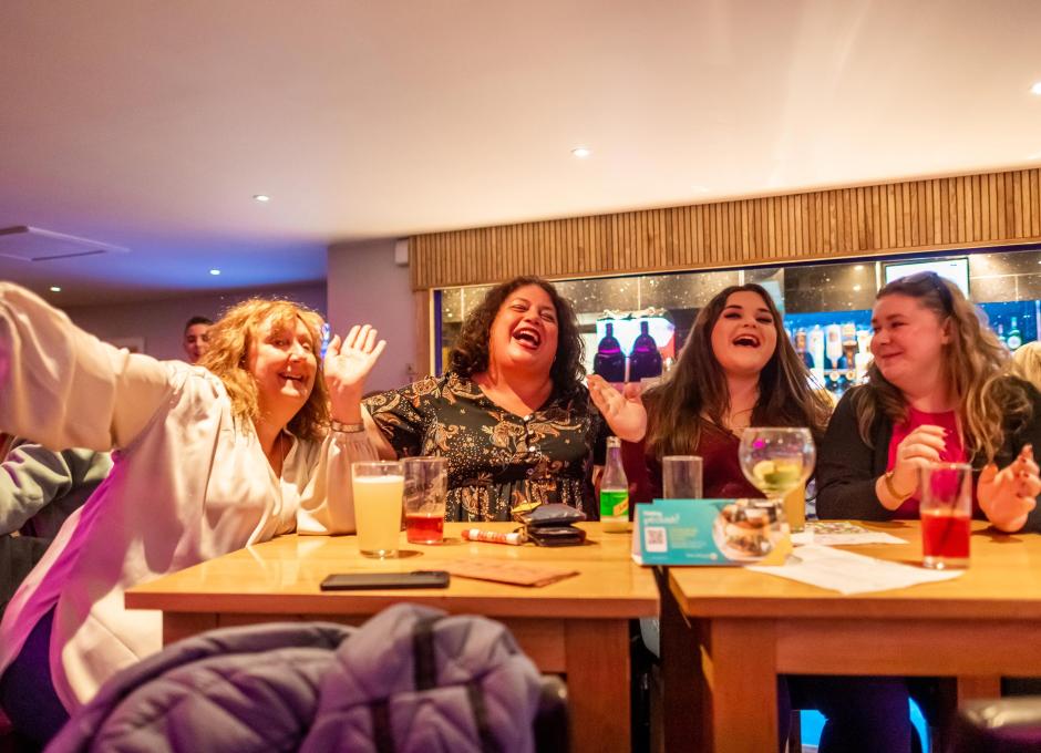 Guests sitting at a table with drinks in the Clubhouse at Woolacombe Sands Holiday Park